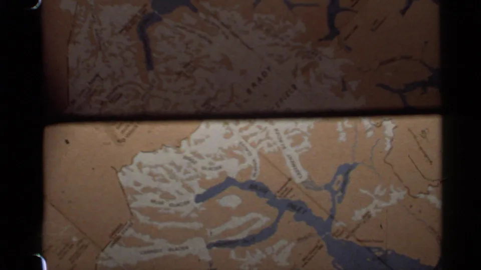 Darker 1977 Alaska 8mm frame showing a sepia map detail with blue waterways, fine labels, and visible sprocket-area borders.