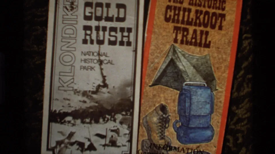 1977 Alaska 8mm frame with a black-and-white Klondike Gold Rush brochure beside a color Chilkoot Trail brochure.