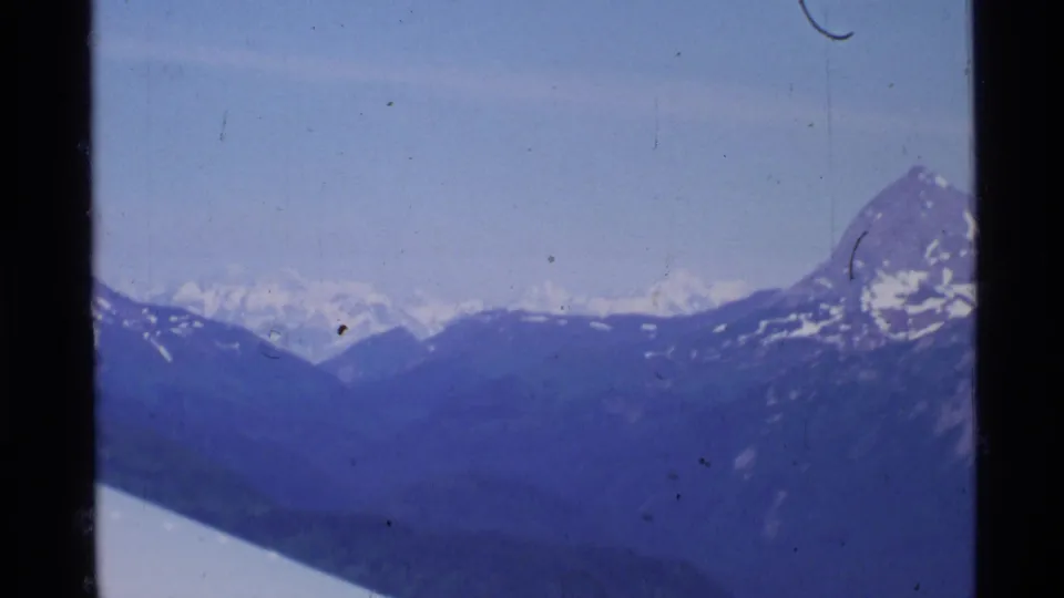 Aerial 8mm view over Alaskan mountain ridges, with a white aircraft wing edge crossing the lower frame.