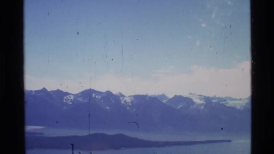 1977 Alaska aerial view of distant ridges, a broad body of water, and low islands through window framing.