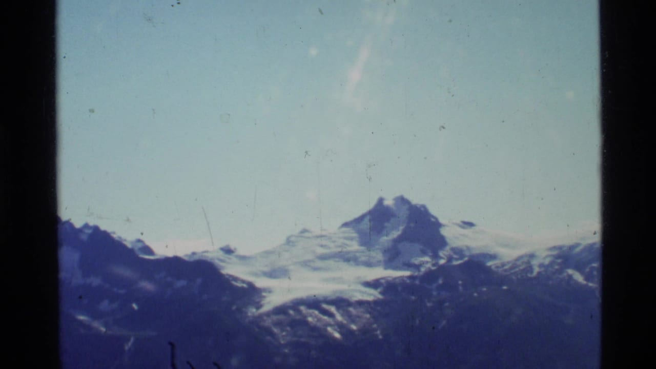 Distant snow-covered mountain peak above dark ridges under a pale blue sky.