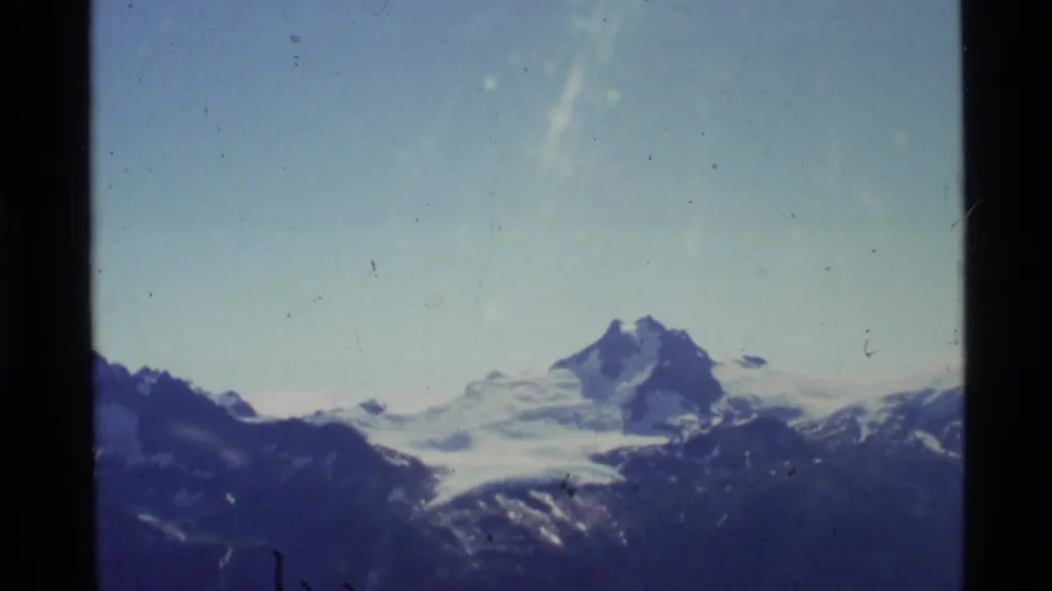 Vintage 8mm view of an Alaskan snow-covered peak with dark mountain ridges and visible film gate edges.