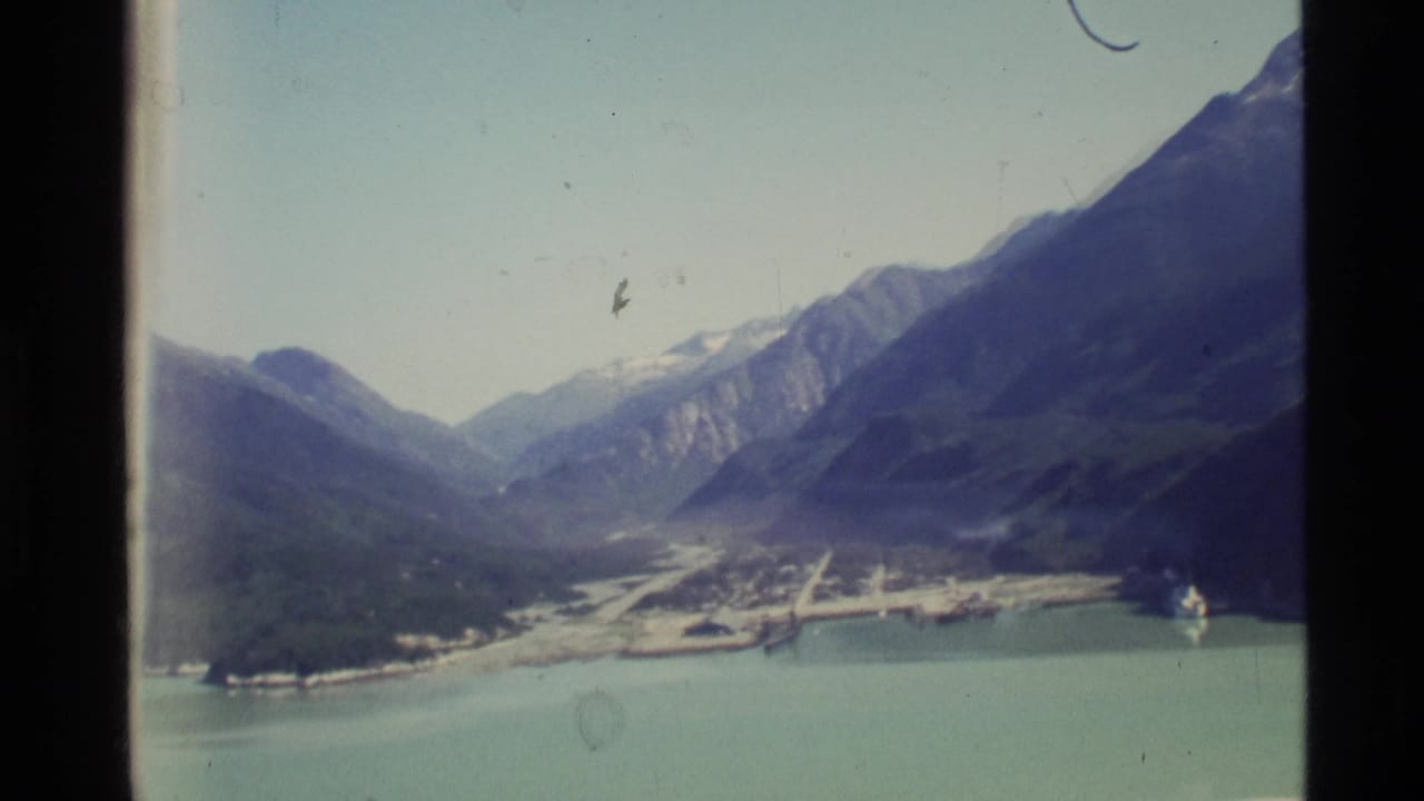 Broad mountain valley with turquoise water, road or settlement area, and distant peaks.