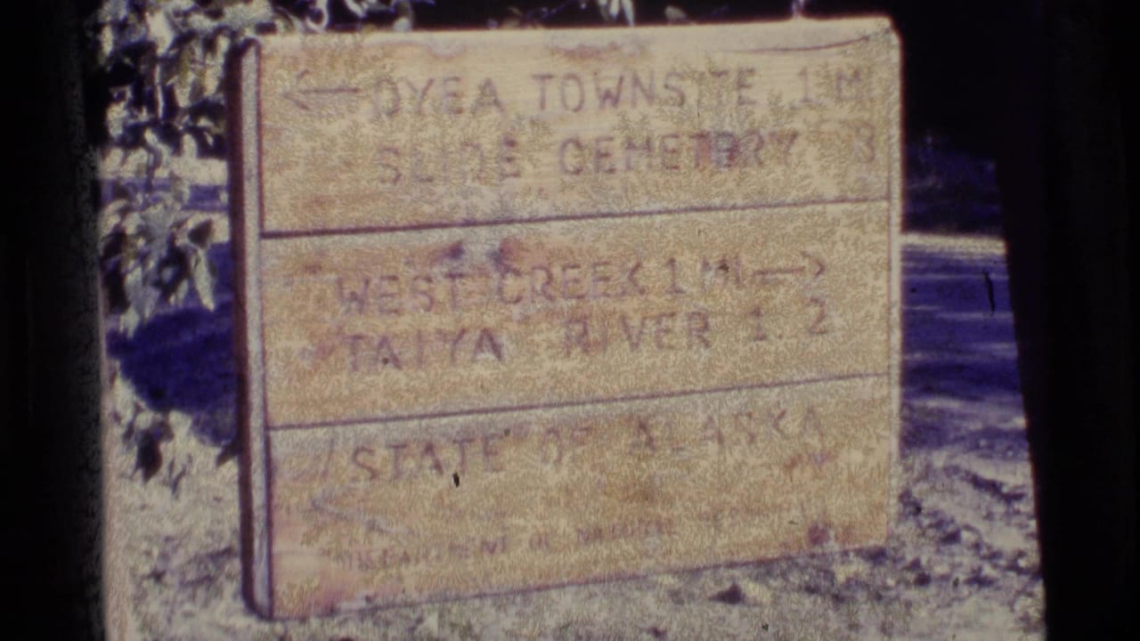 1977 Alaska 8mm frame showing a weathered sign with directions to Dyea Townsite, Slide Cemetery, West Creek, and Taiya River.