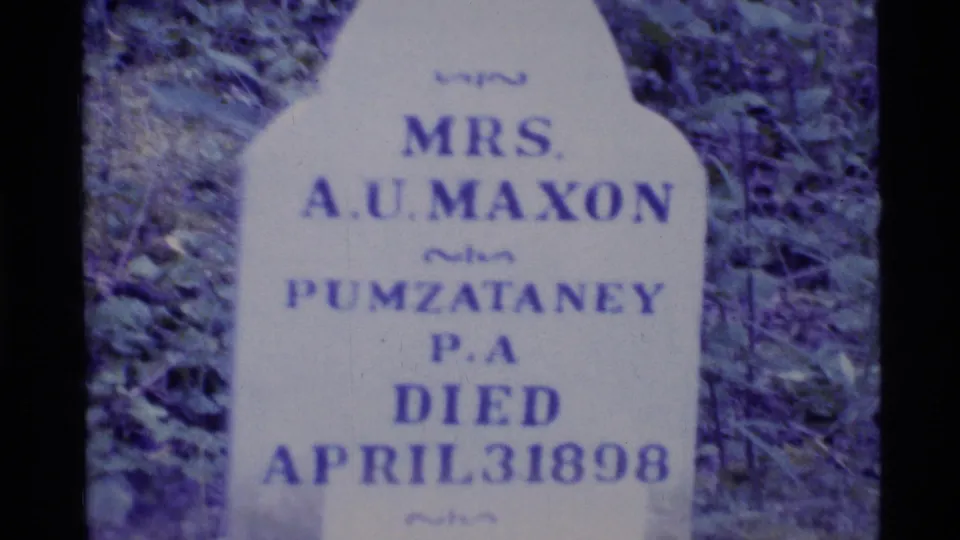 1977 Alaska 8mm close-up of a pale gravestone for Mrs. A.U. Maxon, with vegetation and film grain visible.