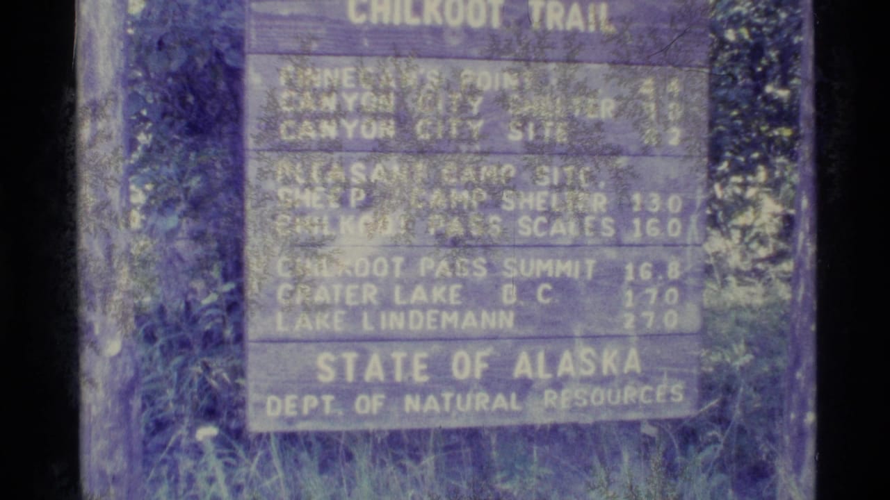 1977 Alaska 8mm frame showing a State of Alaska Chilkoot Trail sign with distances and surrounding vegetation.