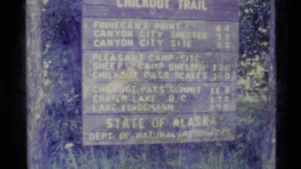 Faded 8mm frame of the Chilkoot Trail distance sign in Alaska, including Canyon City Shelter and Chilkoot Pass Summit listings.