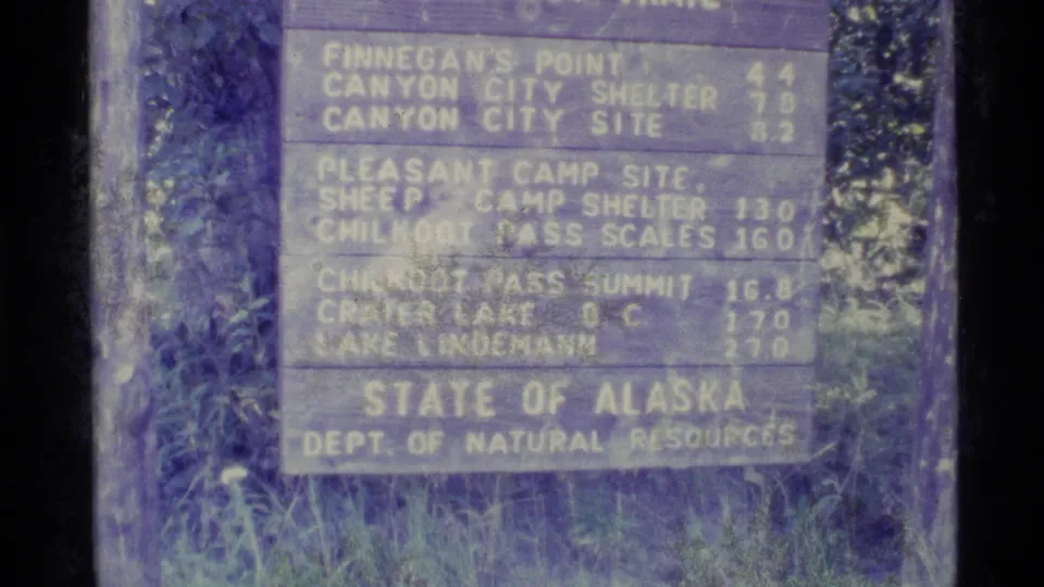 Close 8mm view of the Alaska trail sign, with Finnegan's Point, Canyon City Shelter, and Chilkoot Pass information visible.