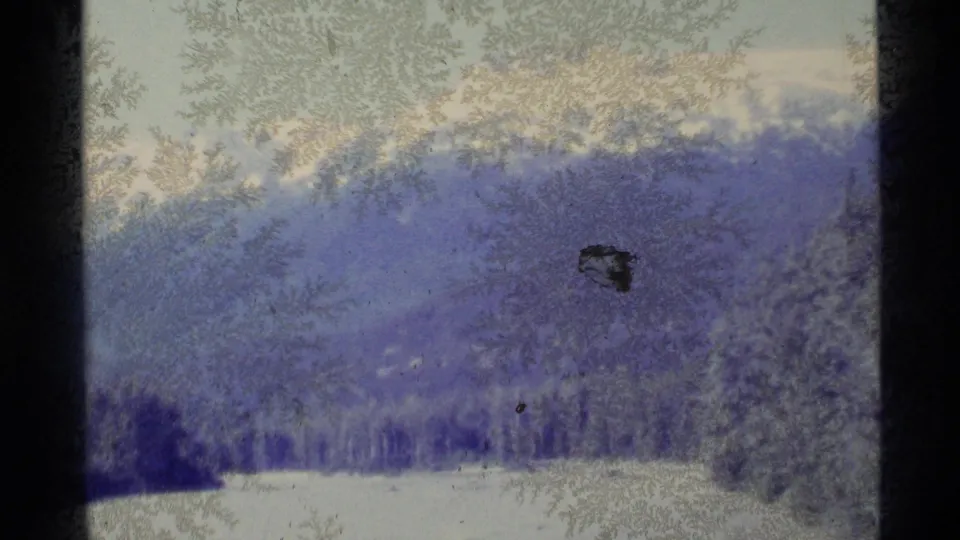 Snowy mountain slopes and a white river plain are seen through soft, grainy 8mm exposure.