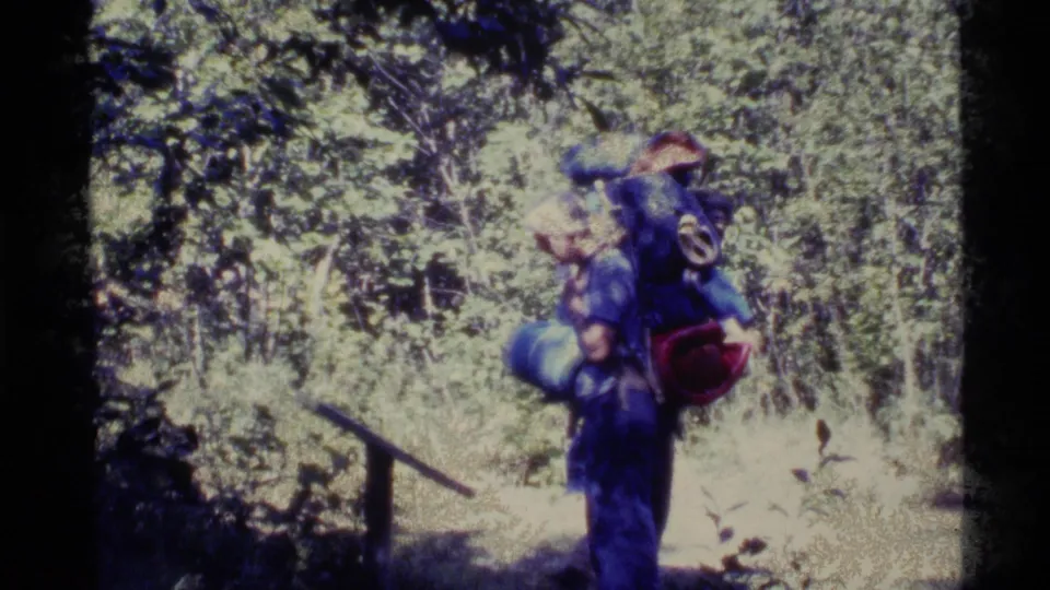 End frame shows hikers with bulky backpacks beside dense forest growth, rendered with strong 8mm grain and color shift.