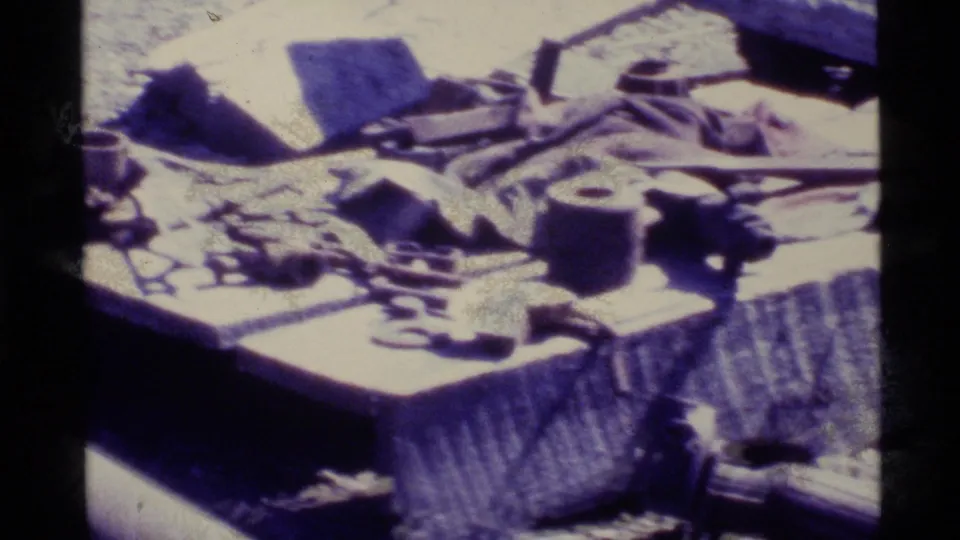 8mm home-movie frame showing a picnic table or flat surface with scattered supplies during an Alaska hiking trip.