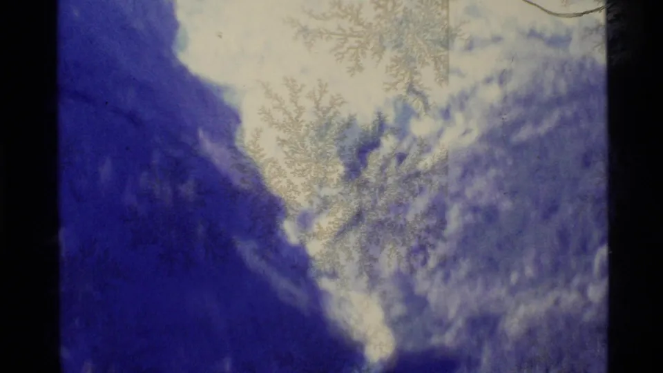 1977 Alaska 8mm frame showing a snowy mountain pass, dark slope, pale sky, and crystalline surface patterns on the film.