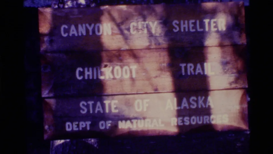 1977 Alaska 8mm frame showing a weathered wooden Canyon City Shelter sign for the Chilkoot Trail, marked State of Alaska.