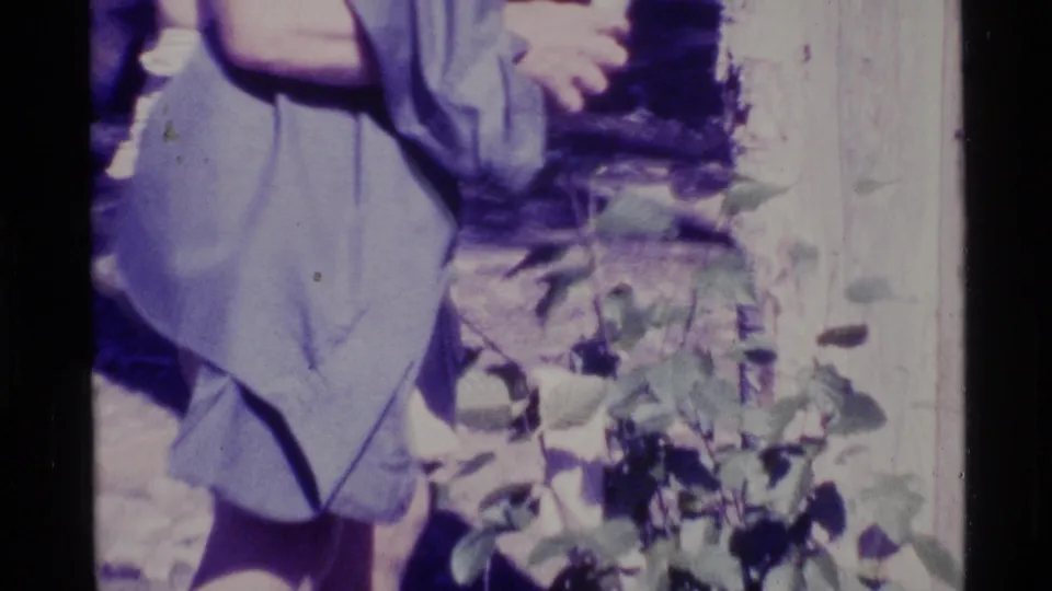 1977 Alaska 8mm frame with a partially seen visitor near the shelter area, foliage, and bright wooden wall or post at right.