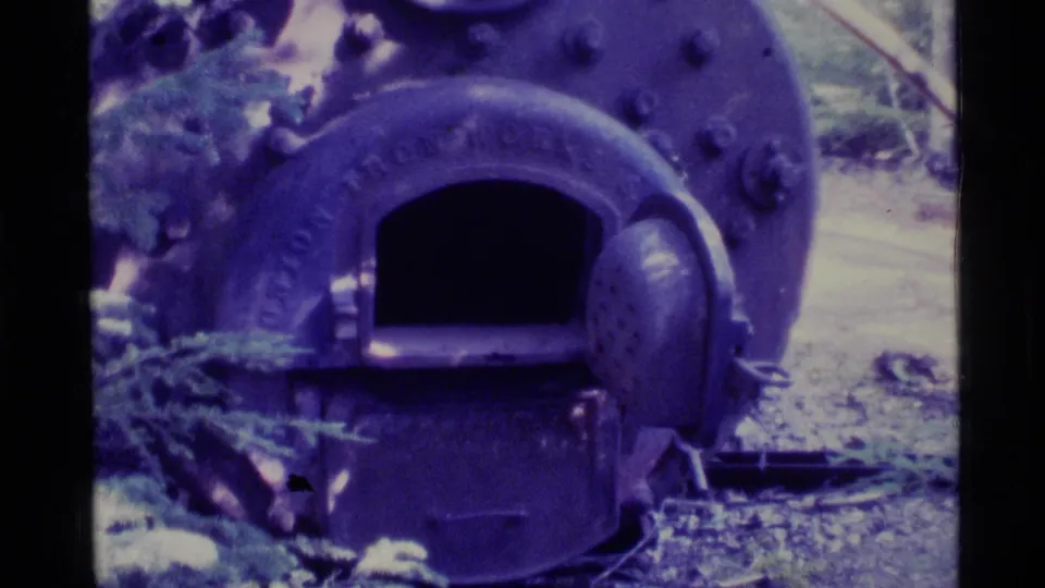 1977 Alaska 8mm frame showing the front plate of a boiler-like metal object with an arched opening and bolts.