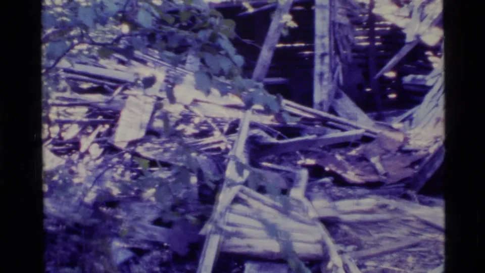 1977 Alaska 8mm frame showing scattered boards, splintered wood, and collapsed structural debris in a ruined cabin area.