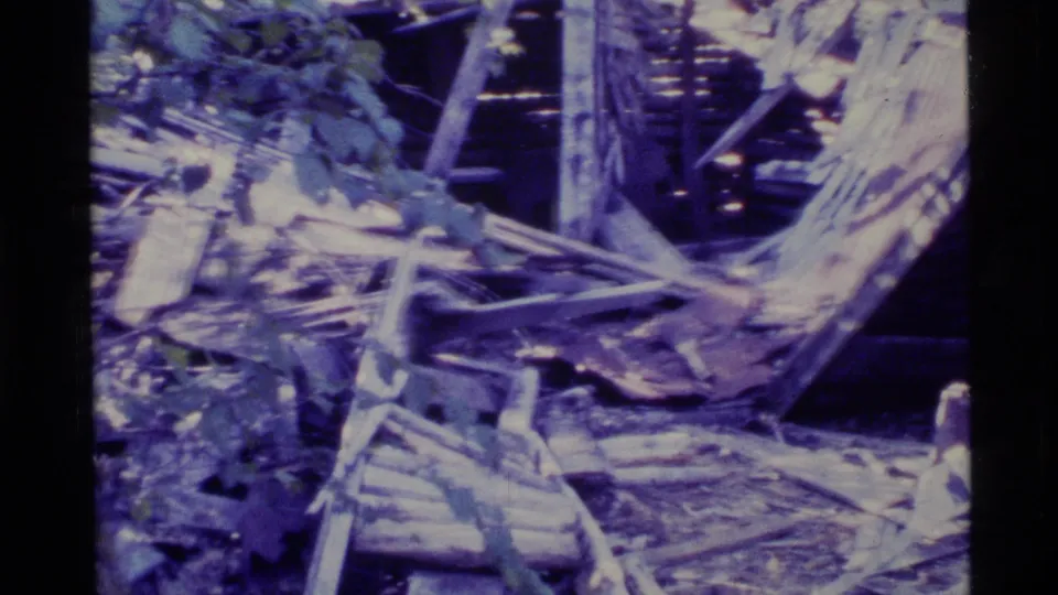 1977 Alaska 8mm frame showing splintered wood, debris, and surrounding trees after a reported rock slide.