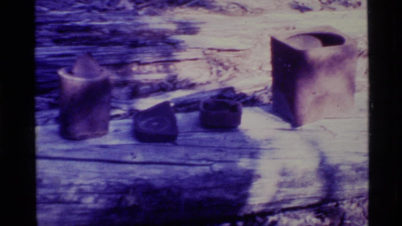 1977 Alaska 8mm frame showing pottery-like vessels and a small dark object on a weathered log in soft, faded color.