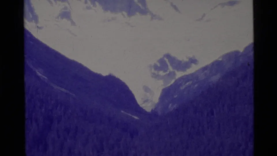 1977 Alaska 8mm view of snowy peaks, a mountain valley, and dark forested slopes with handheld home-movie softness.