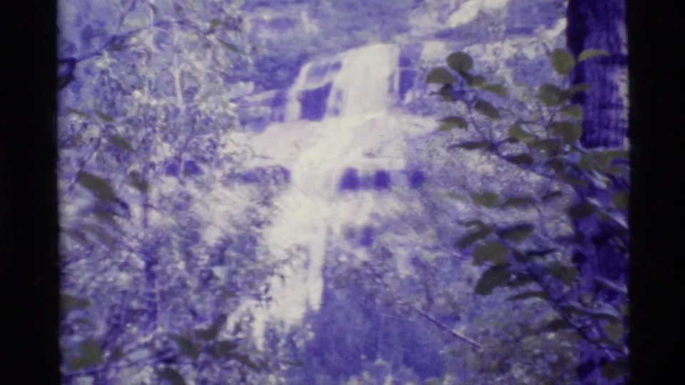 1977 Alaska 8mm frame showing a closer view of white water cascading through a wooded scene.