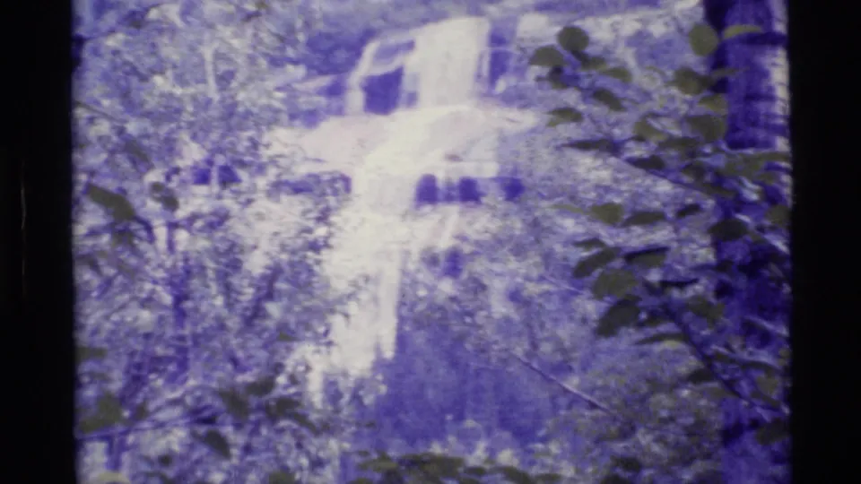 1977 Alaska 8mm frame of a waterfall among trees, with soft focus, grain, and purple-blue color fading.