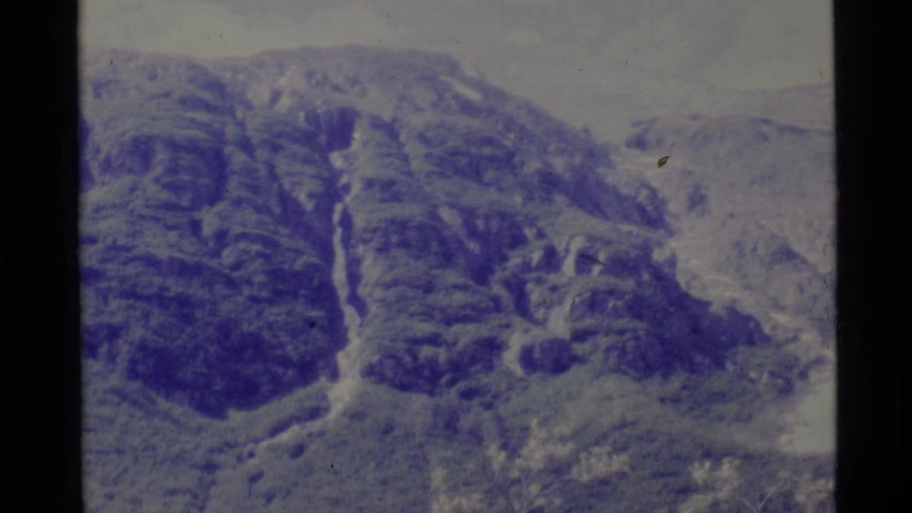 Distant mountain slope with forested ridges and a pale drainage line running downward.