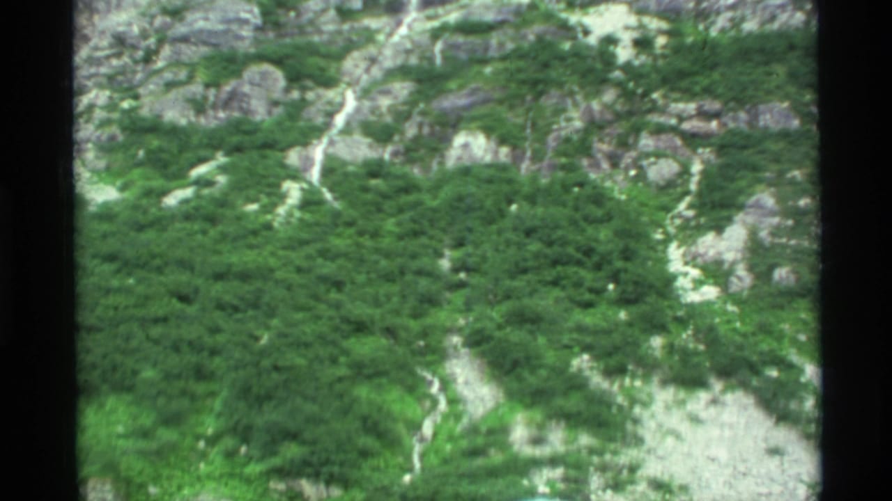 Green rocky mountainside with a narrow waterfall running down the slope.