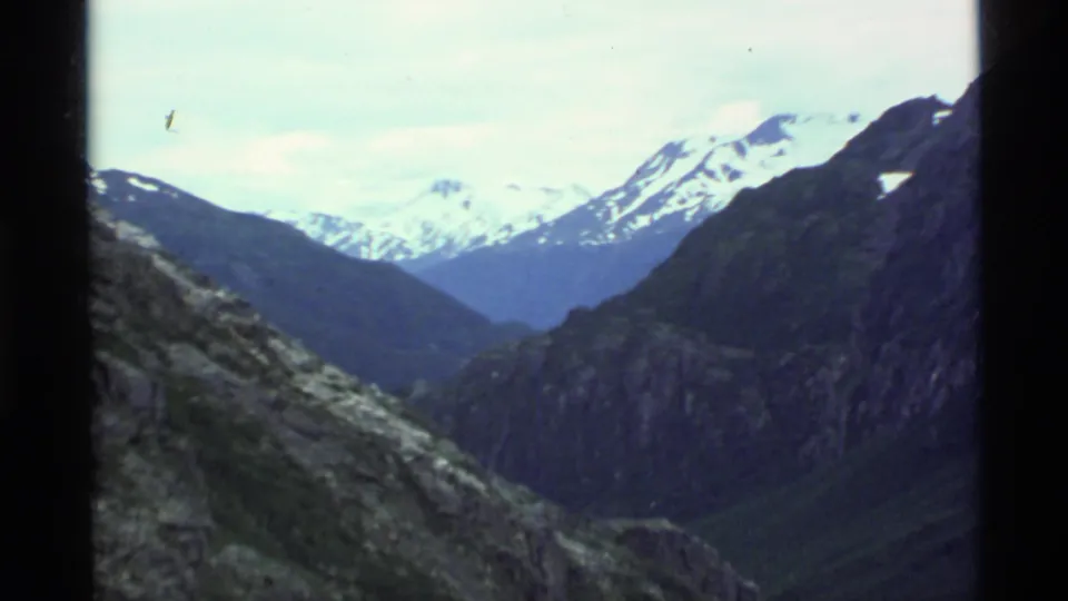1977 Alaska home-movie landscape frame showing a wide rocky valley and distant snow-covered peaks.