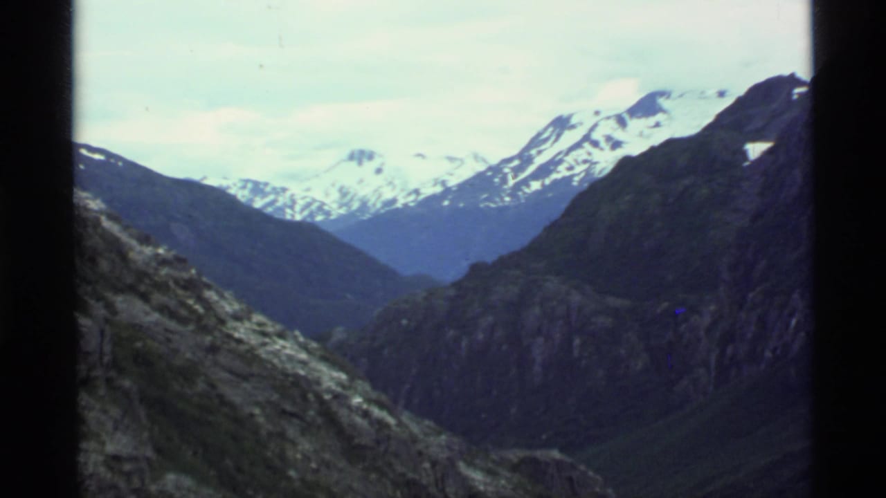 Snow-capped mountains above a dark rocky valley, framed by black film borders.