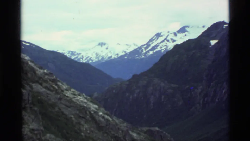 1977 Alaska 8mm view of snow-capped mountain peaks and a shadowed rocky valley seen through projector borders.
