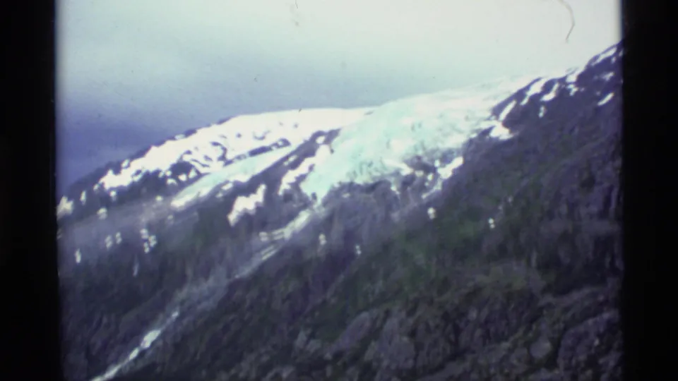 1977 Alaska 8mm frame of a snow-covered ridge above dark rocky slopes, softened by grain and color fading.