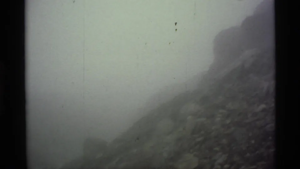1977 8mm Alaska footage shows a foggy rocky slope with muted color, soft focus, and visible film wear.