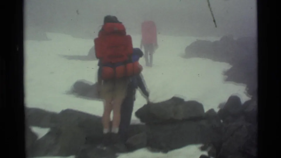 Three hikers continue away through a foggy snowy pass in Alaska, filmed with soft handheld 8mm texture.