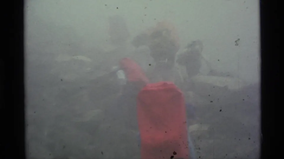 1977 Alaska home-movie frame showing hikers with packs gathered on a rocky slope under dense mist.