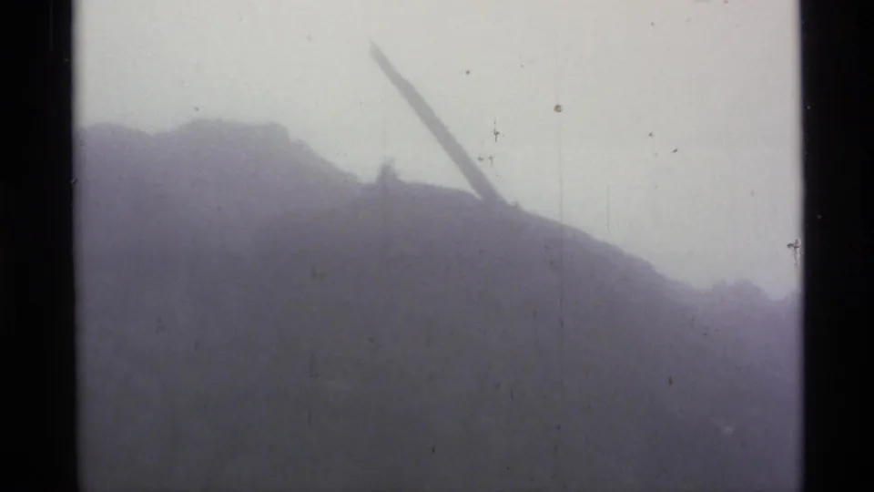 Misty Alaska mountain slope with a dark ridge line and a diagonal branch or pole in faded 8mm footage.