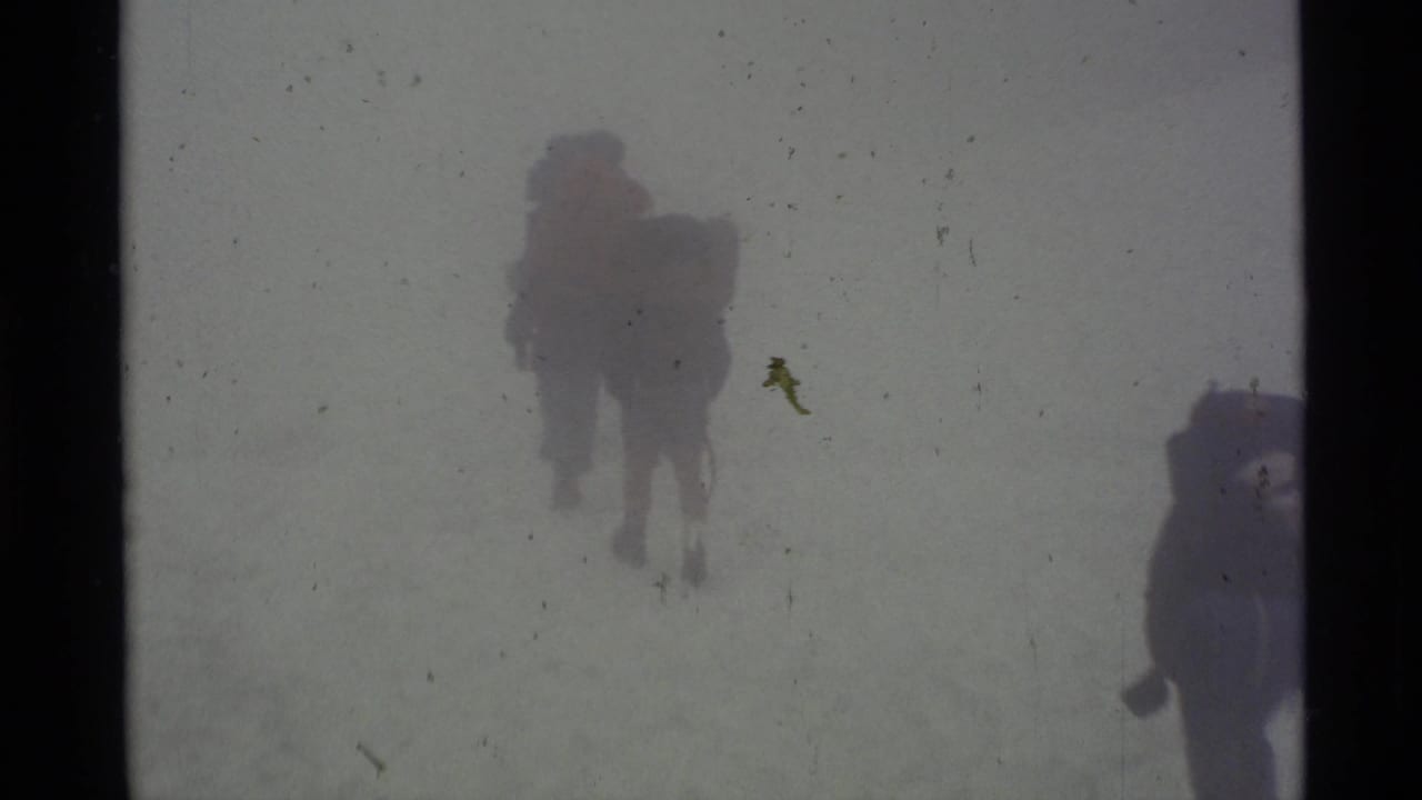 1977 Alaska 8mm frame showing hikers with large packs moving through heavy mountain fog across snow.