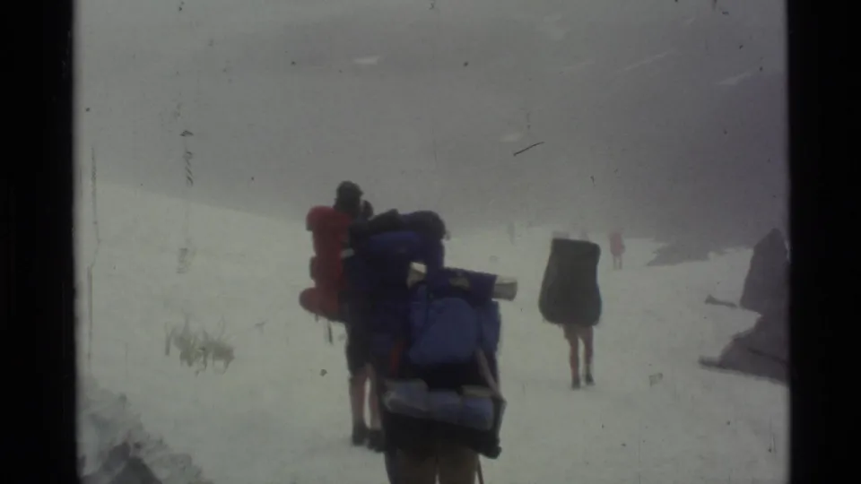 A backpacker in bright outerwear crosses a foggy Alaskan snowfield, with other hikers barely visible ahead.