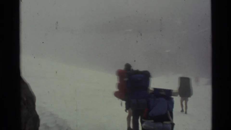 1977 Alaska home-movie footage shows hikers moving along a snowy route with fog obscuring the mountain setting.