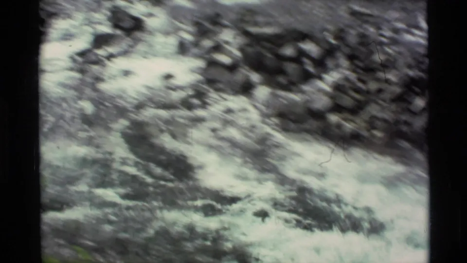 Close 8mm view of turbulent Alaskan stream water moving over dark rocks, with handheld motion blur.