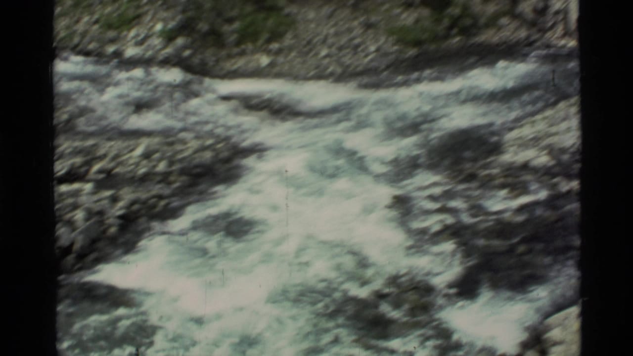 1977 Alaska 8mm frame showing pale rushing water moving through rocky terrain, bordered by the scanned film edge.