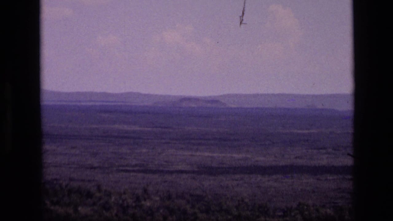 1972 Idaho 8mm frame showing a broad hazy plain with low distant mountains and a pale sky, bordered by dark film gate edges.