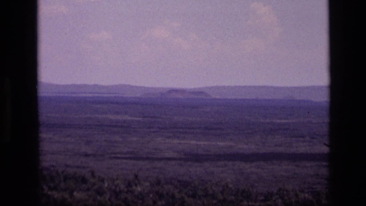 1972 Idaho landscape frame with a flat open plain, distant low mountains, pale sky, and visible dark 8mm frame borders.