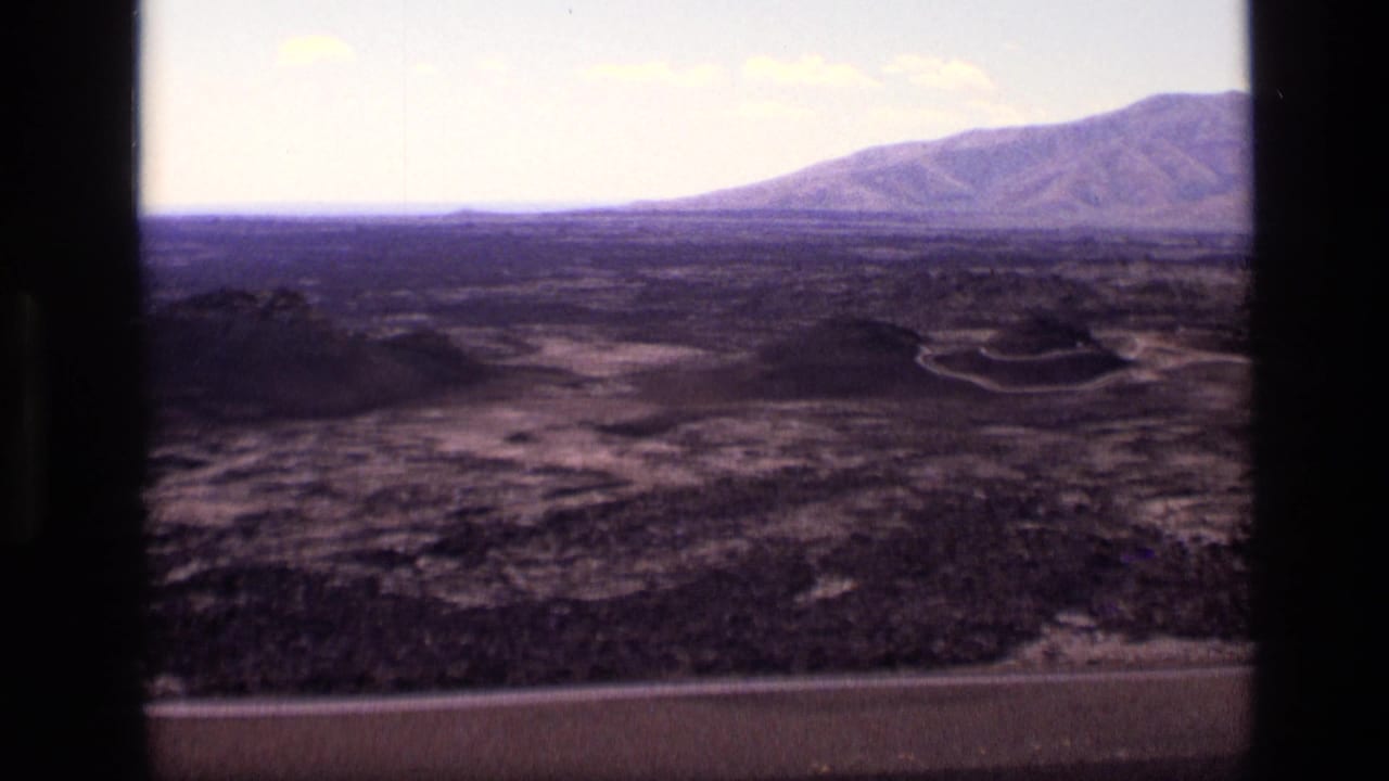 Volcanic landscape seen through a dark car window with distant mountain and broad horizon.