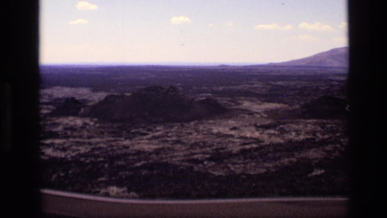 Wide volcanic terrain with low dark hills and car-window framing at the sides.