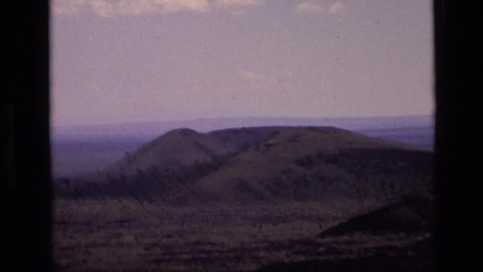 1972 Idaho 8mm frame showing rounded grass-covered hills and faint distant landforms beneath a soft, pale sky.