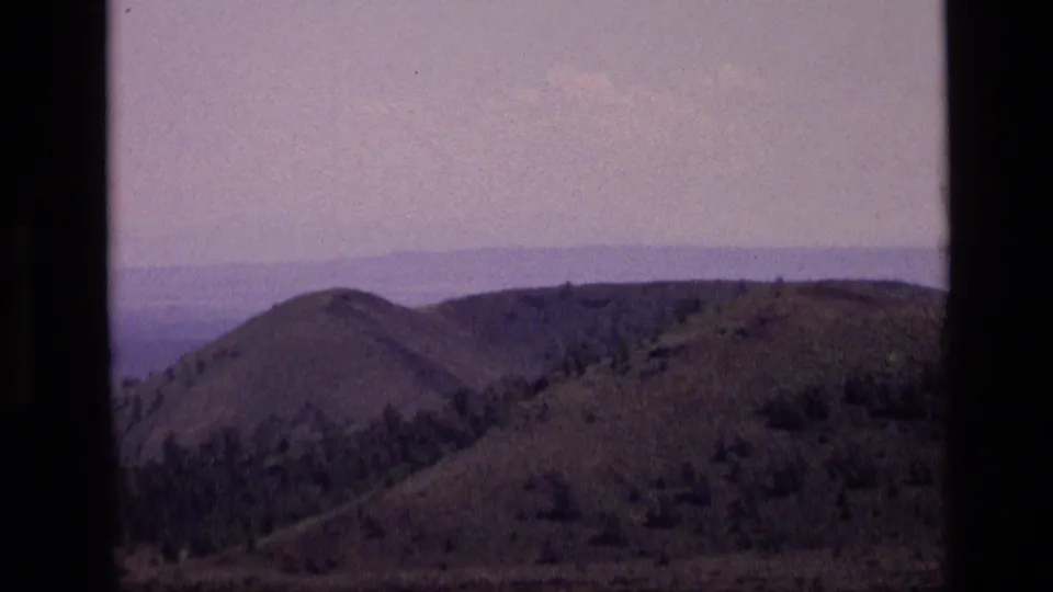 1972 Idaho 8mm frame with a zoomed view of rolling hills, scattered vegetation, and a distant horizon line.