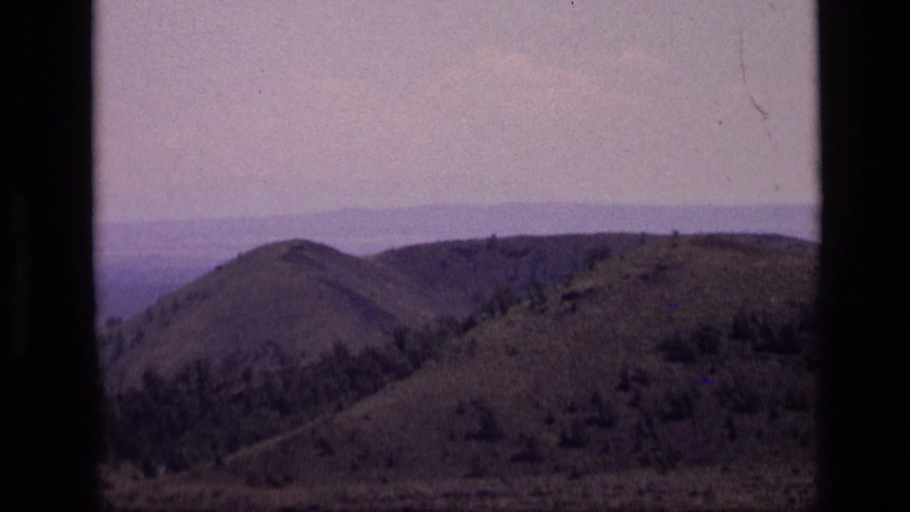 Wide view of rolling hills under a hazy sky, bordered by dark film edges.