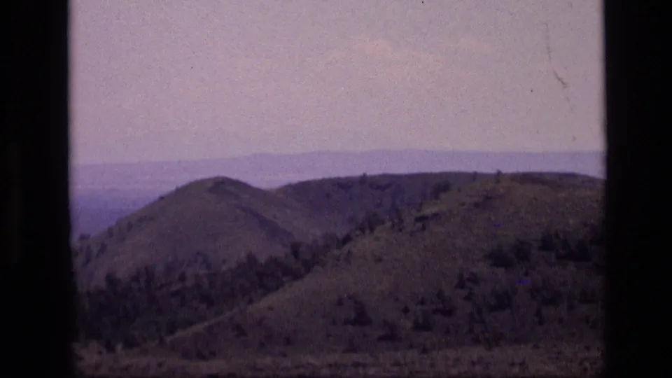 1972 Idaho home-movie frame showing rolling hills and distant ridges under a hazy sky, with visible 8mm gate edges.