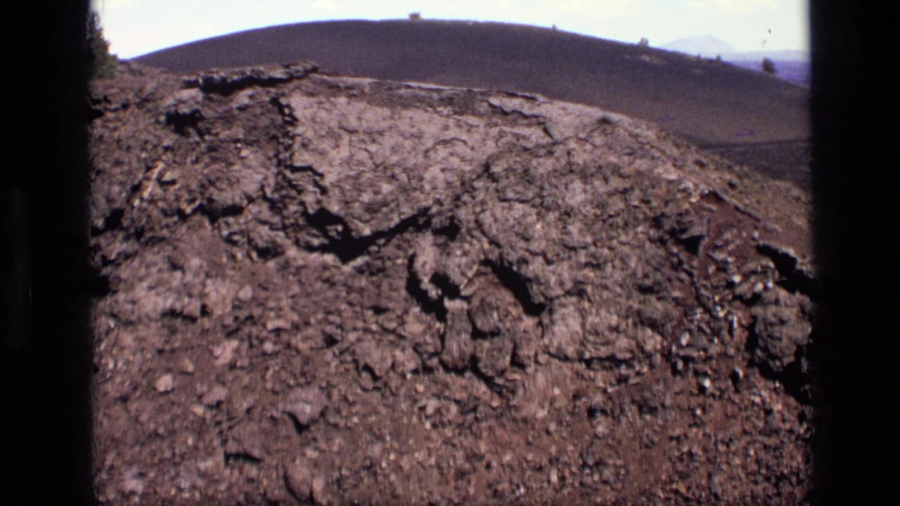 Cracked rocky ground in the foreground with a rounded hill and pale sky beyond.