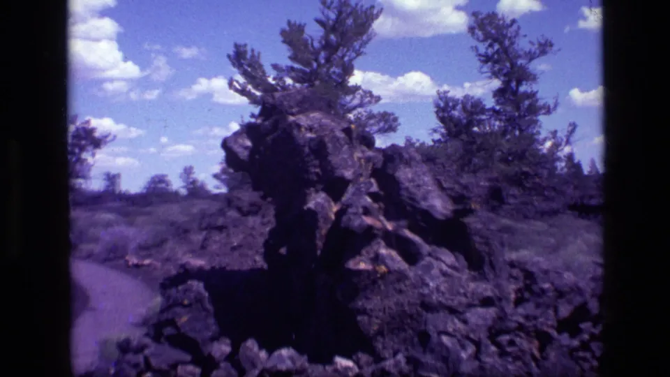 1972 Idaho home-movie frame of a rugged rock formation framed by pines, open sky, and visible 8mm film borders.